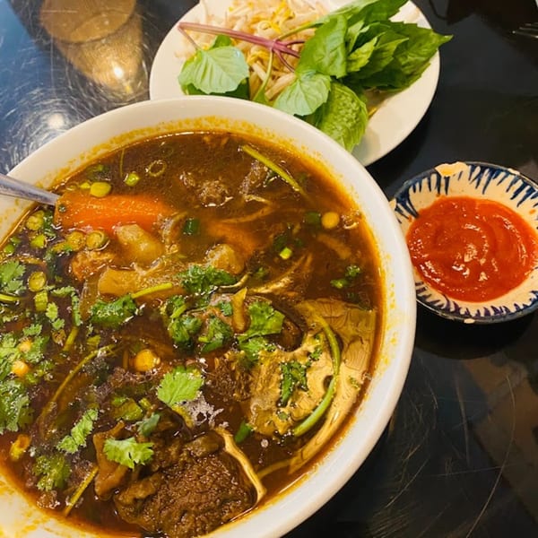 A bowl of Vietnamese beef stew with carrots, cilantro, and a side of bean sprouts and basil.
