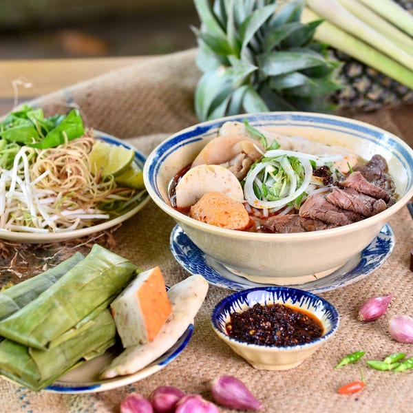 Vietnamese Bun Bo Hue soup with beef, pork, and fresh herbs, served with chili sauce.