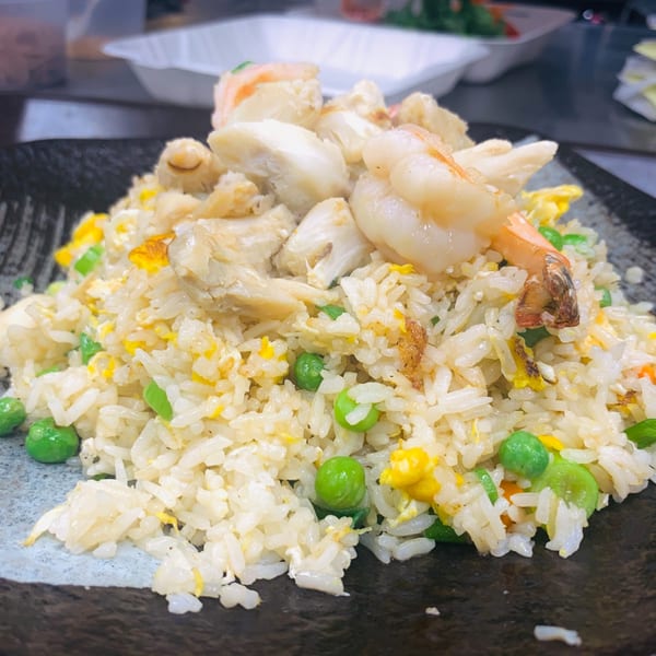 Close-up of seafood fried rice with shrimp, crab meat, peas, and scrambled egg on a dark plate.
