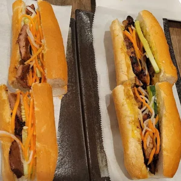 Four Vietnamese banh mi sandwiches with meat, pickled carrots, and daikon on a dark tray.