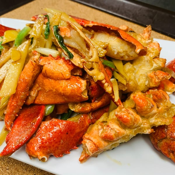 Close-up of stir-fried lobster with ginger and scallions on a white plate.