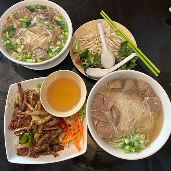 Vietnamese pho with beef, meatballs, and stir-fried beef with onions, alongside fresh garnishes.