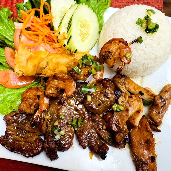 A Vietnamese combo plate with grilled pork, chicken, shrimp, egg roll, rice, and fresh vegetables.
