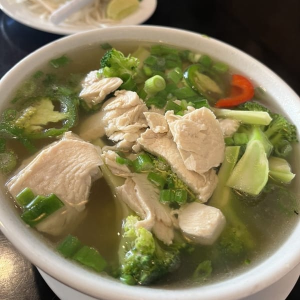 Close-up of a Vietnamese chicken pho with broccoli, jalapenos, and green onions in a white bowl.